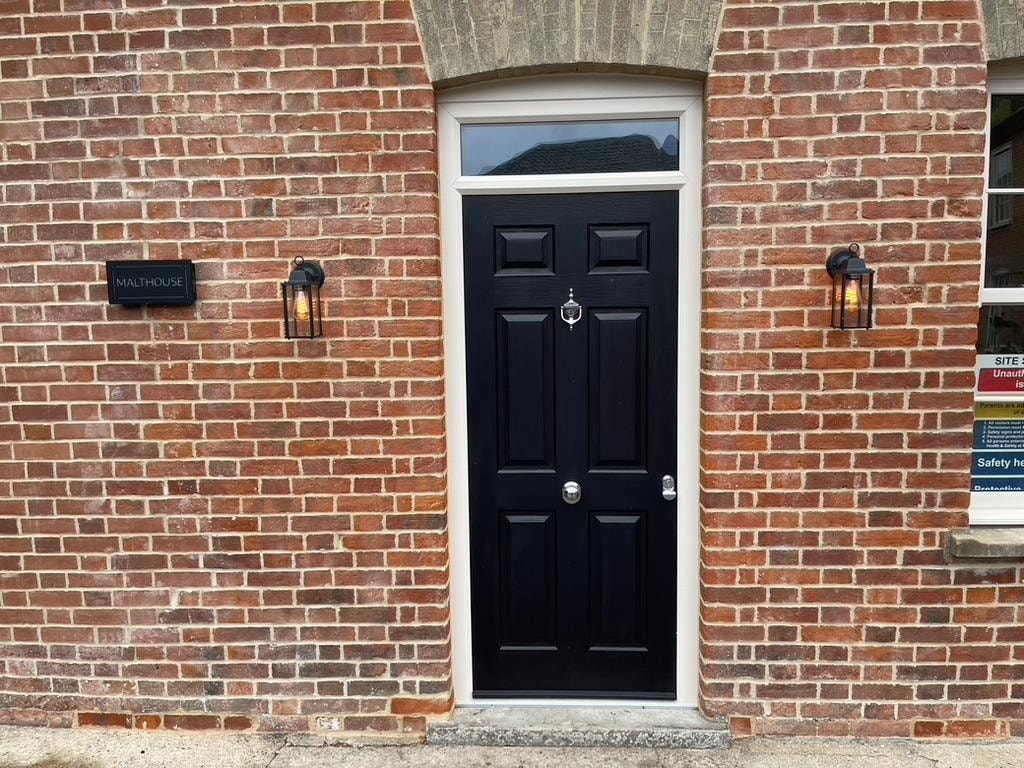 Malthouse refurbishment — restored brick entrance with black door and lanterns